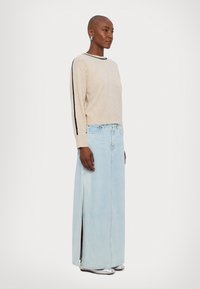 Bežna pletena jopica z črnimi stranskimi črtami, v kombinaciji s svetlo modrim denim maxi krilom. Krilo ima stranski razporek; model nosi srebrne balerinke.