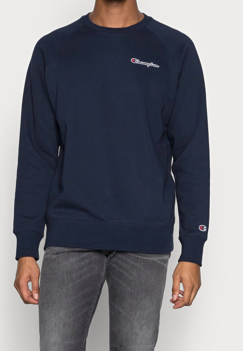 Námořnický modrý svetr se švy raglán, elastickými manžetami a lemem, s malým logem Champion na hrudi a na rukávu. Vyrobeno z měkkého materiálu.