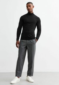 Suéter negro de cuello alto, de corte ajustado, combinado con pantalones de cuadros en gris claro. El modelo lleva zapatillas blancas y está de pie sobre un fondo neutro.