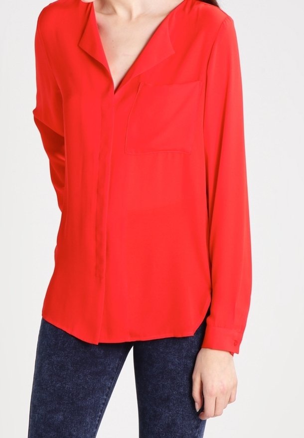 Blusa rossa a maniche lunghe con colletto, tasca frontale e orlo dritto. Realizzata in tessuto morbido con una leggera lucentezza.