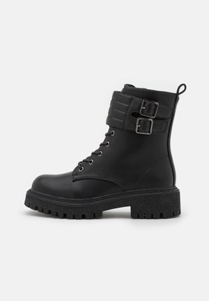 Bottine noire en cuir avec tige texturée, deux bouclettes décoratives, bout rond, fermeture à lacets à l'avant et semelle en caoutchouc épaisse à crampons prononcés.