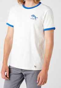 Vit bomull T-shirt med blå ribbad krage och ärmslut. Har en blå hästgrafik och "Wrangler" text på framsidan.