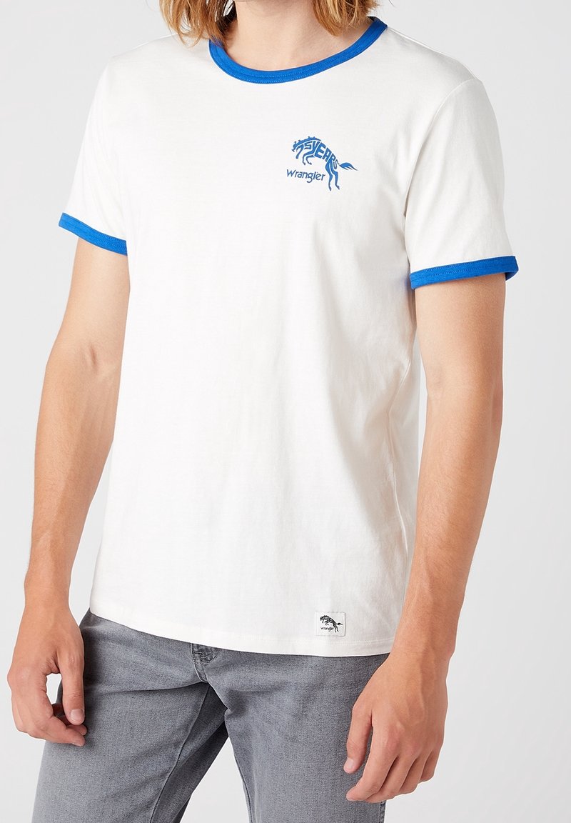 Vit bomull T-shirt med blå ribbad krage och ärmslut. Har en blå hästgrafik och "Wrangler" text på framsidan.