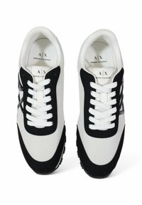 Baskets athlétiques blanches et noires en mesh et en suède, avec un bout arrondi, des lacets blancs et un logo argenté sur le côté.