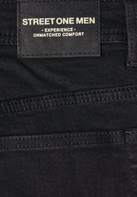 Tejido de mezclilla negra con costuras cosidas y una etiqueta de cuero negro cosida que dice "STREET ONE MEN - EXPERIENCE - UNMATCHED COMFORT".