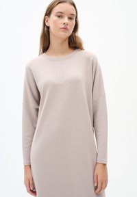 Haljina dugih rukava, opuštenog kroja, izrađena od mekanog, svijetlog bež materijala. Sadrži okrugli izrez i minimalistički dizajn, s lagano prozračnom siluetom.