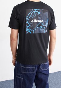 Černé tričko s velkým potiskem v modré a šedé na zadní straně, s nápisem "ellesse" vytištěným v bílé. Krátké rukávy, volný střih.