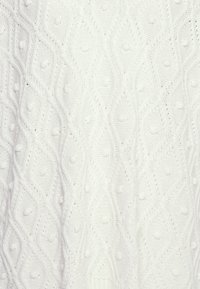 Suéter blanco de punto con un patrón de diamantes que presenta texturas en relieve y pequeños detalles de bolitas a lo largo de la tela.