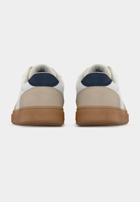 Λευκά αθλητικά παπούτσια με μπεζ λεπτομέρειες και ναυτικό μπλε ταμπελάκι στη φτέρνα. Λείος δερμάτινος επάνω μέρος, υφασμένη φτέρνα, και διαφανής σόλα από καουτσούκ. Κλασικός χαμηλός σχεδιασμός.