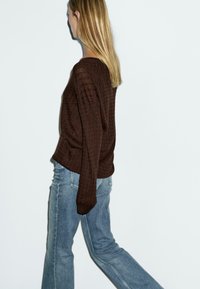 Brun strikket sweater med et struktureret mønster, parret med lyseblå jeans. Sweateren har en afslappet pasform og lange ærmer.