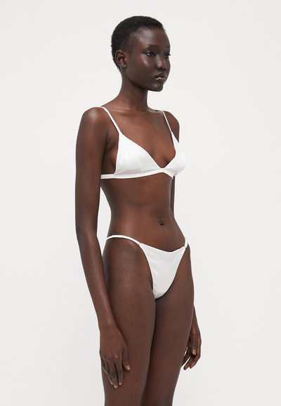 Set di bikini bianco composto da un reggiseno con spalline sottili a forma triangolare e uno slip a vita bassa abbinato, realizzato in tessuto morbido con dettagli minimi.