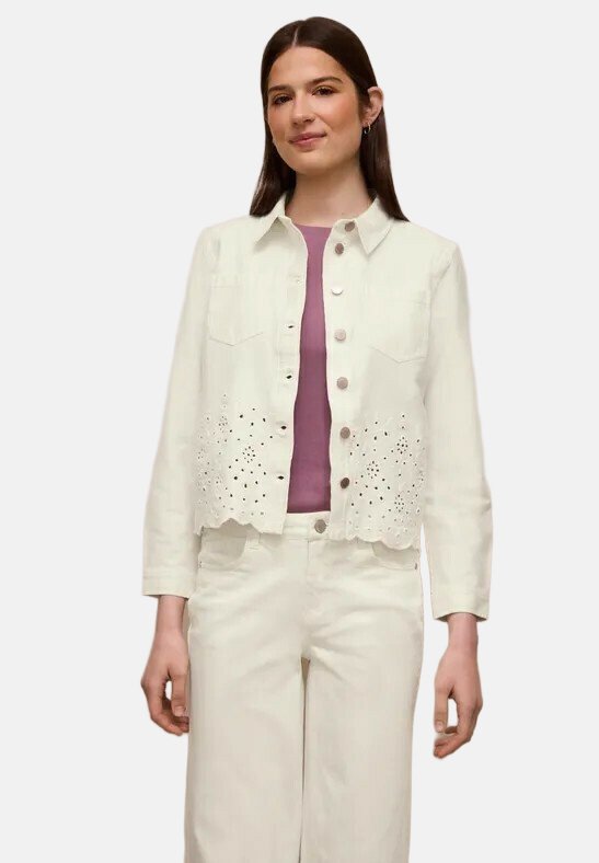 Jeune femme portant une veste blanche boutonnée avec un motif floral en découpe sur un top mauve et un pantalon blanc assorti.