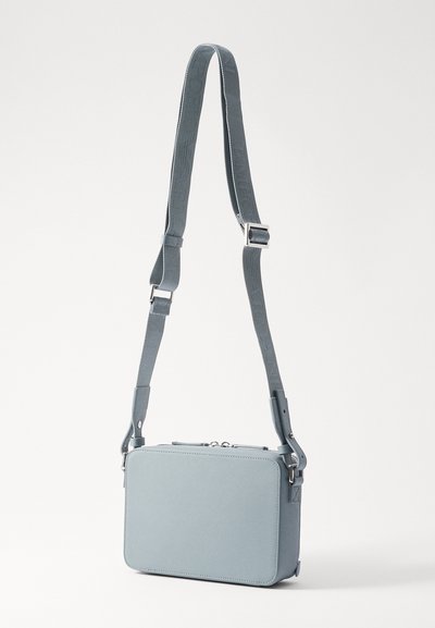 Geantă crossbody rectangulară din imitatie de piele bleu deschis, cu curea detasabilă ce prezintă un model cu logo și accesorii din metal argintiu.