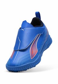 Zapatilla deportiva azul con un upper liso y texturizado. Cuenta con una correa de gancho y bucle, acentos rojos contrastantes y una suela de goma con patrón de tracción.