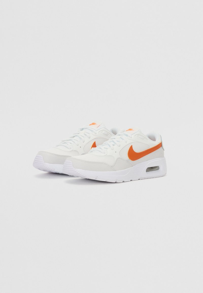 Zapatilla blanca con el swoosh de Nike en naranja, material de malla y cuero, cuello acolchado, puntera redonda y unidad de aire visible en la suela.