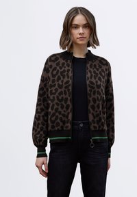 Hnědý kardigan s leopardím vzorem, čern�ým límcem, zapínáním na zip a zeleným proužkovaným lemem. Nošený přes černé tričko a tmavé džíny.