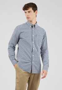 Camicia a quadri blu marina e bianca in cotone, con taschino sul petto, maniche lunghe e colletto classico. Texture liscia e vestibilità su misura.