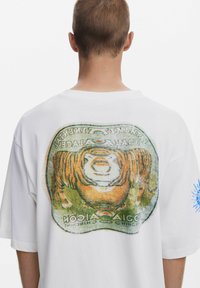 Balta medvilninė marškinėliai su per dideliu kirpimu. Užpakalinėje pusėje yra spalvinga tigro grafika ir prekės ženklo detalė. Trumpi rankoviai ir standartinė apvalia apykakle.