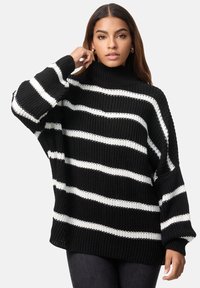 Schwarz-weiß gestreifter Strickpullover mit hohem Kragen, lockerer Passform und gerippten Ärmel- und Saumdetails. Die Textur wirkt dick und gemütlich.