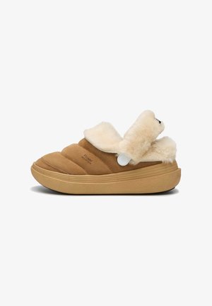 Scarpe slip-on in camoscio marrone con colletto in pelliccia cremosa, suola testurizzata e dettaglio con bottone, progettate per comfort e facilità d'uso.