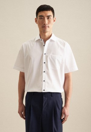 Chemise blanche à manches courtes avec une poche poitrine et des boutons navy. Texture lisse, col classique et détails de motif intérieur subtils.