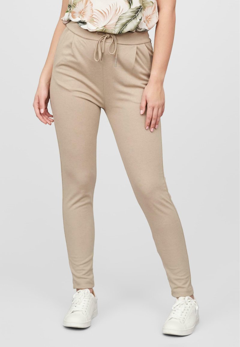 Beige joggebukser laget av myk stoff, med snor i livet og en smal passform. Kombinert med hvite sneakers.