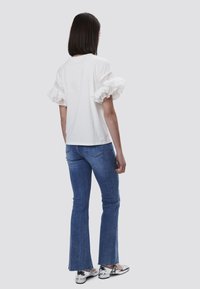 Hvid t-shirt med bølgede, stribede ærmer, parret med blå flagrende jeans og metaliske sølv sko. Glat tekstur og afslappet pasform.