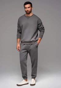Sudadera gris y joggers hechos de una tela suave. La sudadera tiene un cuello redondo y puños acanalados; los joggers tienen tobillos elásticos y bolsillos.