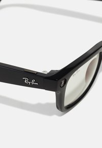 Lunettes intelligentes Ray-Ban noires avec une épaisse monture rectangulaire et un petit objectif de caméra sur le coin avant de la branche droite.