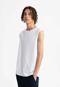 Witte mouwloze katoenen t-shirt met een ronde halslijn, losse pasvorm en een gladde textuur, gecombineerd met marineblauwe broeken.