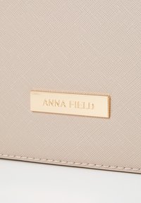 Beež tekstuuriga rahakott kullast "ANNA FIELD" logo plaadiga. Omab peeneid mustreid ja õmblusi äärealadel. Kompaktne disain.