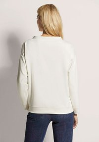 Crème kleurige sweatshirt met lange mouwen, een relaxte pasvorm, ronde hals, ribgebreide manchetten en een gladde textuur, gecombineerd met donkere jeans.
