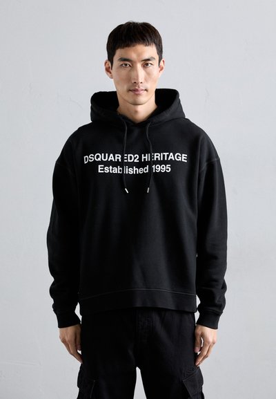 Black cotton hoodie featuring white text "DSQUARED2 HERITAGE Established 1995" across the chest, with a drawstring hood and ribbed cuffs.