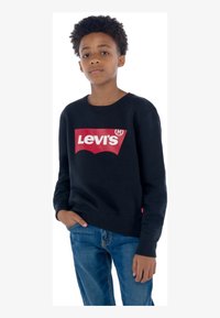 Svart hettegenser laget av bomull med rund hals. Har en stor rød Levi's-logo på fronten. Kombinert med blå denimjeans.