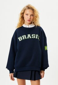 Navyblaues, übergroßes Sweatshirt mit "BRASIL" in fetten grünen Buchstaben, mit einem Patch der brasilianischen Flagge auf dem linken Ärmel. Material aus Baumwollmischung.