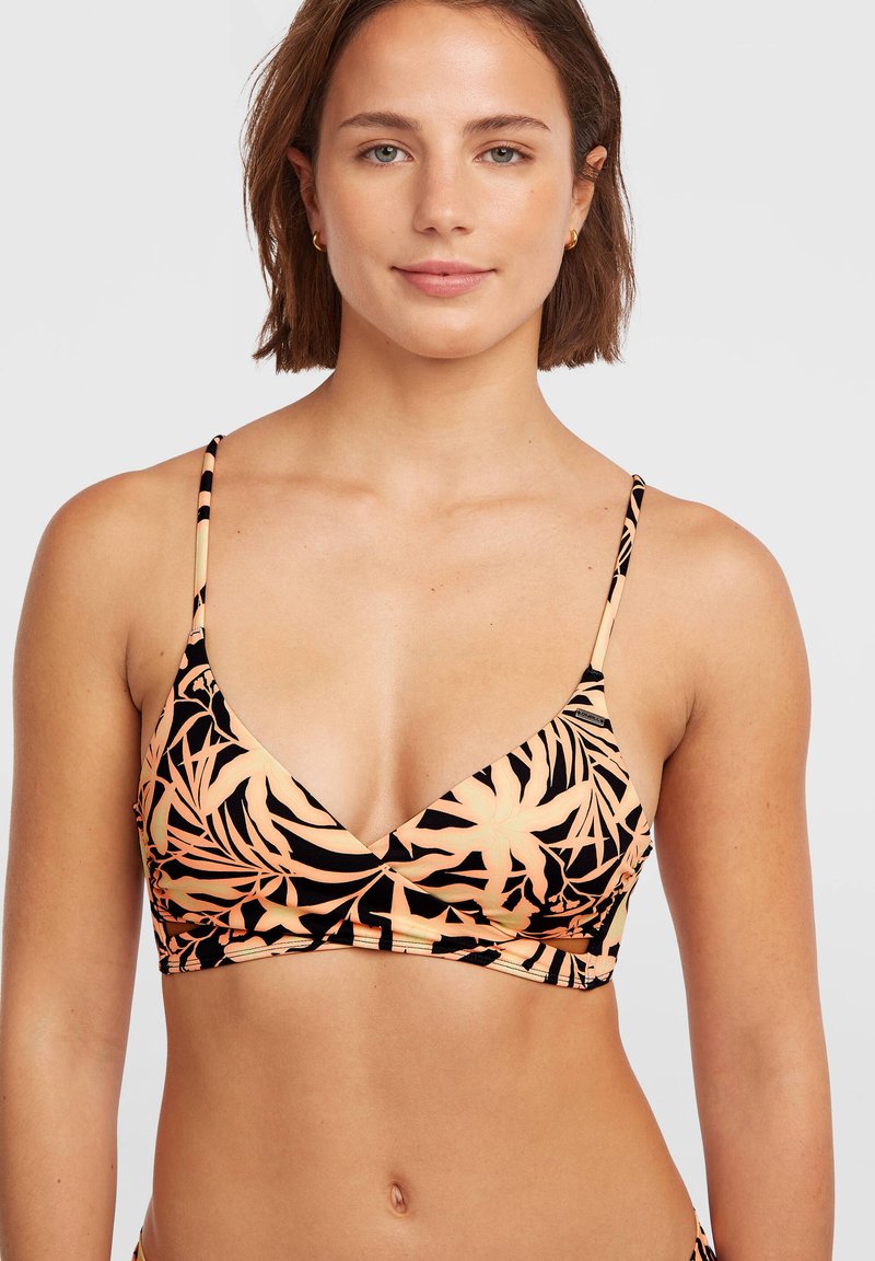 Γυναίκα με κοντά καστανά μαλλιά, που φοράει τοπ μπικίνι με μαύρο και ροδακινί φλοράλ σχέδιο και λεπτές τιράντες, σε απλό ανοιχτό φόντο.