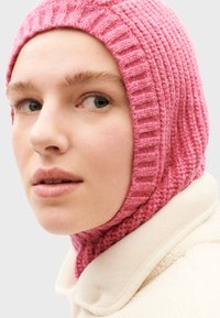 Lyserød strikket balaclava med ribbet tekstur, tætsiddende omkring ansigtet, parret med en cremet fleecekrave.