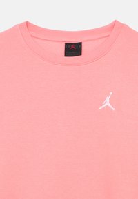 Ροζ βαμβακερό T-shirt με κοντά μανίκια και στρογγυλή λαιμόκοψη, με το λευκό λογότυπο Jordan στο αριστερό μέρος του στήθους και μαλακό, λείο ύφασμα χωρίς υφή.