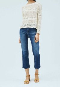 Pull léger en maille avec rayures horizontales, associé à un jean bleu raccourci et des sandales à talons beige. Texture douce et tissage ouvert.