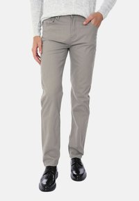 Chino in cotone beige con vestibilità slim, dotati di tasche anteriori e zip. Indossati con scarpe in pelle nera.