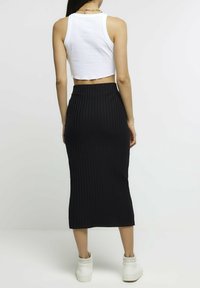 Biały krótki top na ramiączkach zestawiony z czarną prążkowaną spódnicą midi o dopasowanym kroju i wysokim stanem, uzupełnione białymi trampkami.