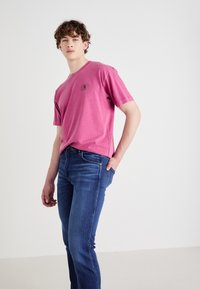 Katoenen T-shirt in levendig roze met een klein logo op de borst; gecombineerd met blauwe denim jeans met een slim fit en klassieke zakken.