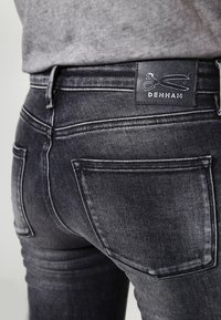 Denham svarta denimjeans har en smal passform, subtila blekningar och en logotyp med saxar på märket. De har en klassisk femficksdesign.