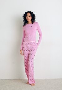 Roze langemouw-top met kleine ontwerpen en bijpassende roze broek met een herhaald patroon van kleine gekleurde iconen. Zacht materiaal, aansluitende stijl.
