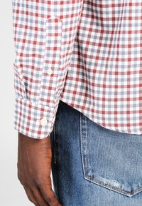 Rutig skjorta i rött och vitt med blå detaljer, i bomullstyg, med knäppta ärmslut, kombinerad med blå denimjeans med synlig sömnad.