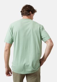 Camiseta de algodón de manga corta en verde menta con cuello redondo, textura suave y corte relajado. Presenta un dobladillo recto y costuras limpias en la parte posterior.