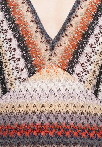 Megztinis su V-kaklu, su daugiamačiais zigzagų raštais raudona, oranžine, violetine ir juoda spalvomis, praturtintas metaliniais siūlais.