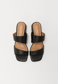 Chanclas negras con dos tiras anchas y un tacón bajo. Fabricadas en cuero suave con una plantilla acolchada en tono marrón.