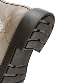 Zapato de ante color beige claro con suela de goma oscura que presenta un patrón de relieve en la suela y un sutil detalle de costura a lo largo del costado.