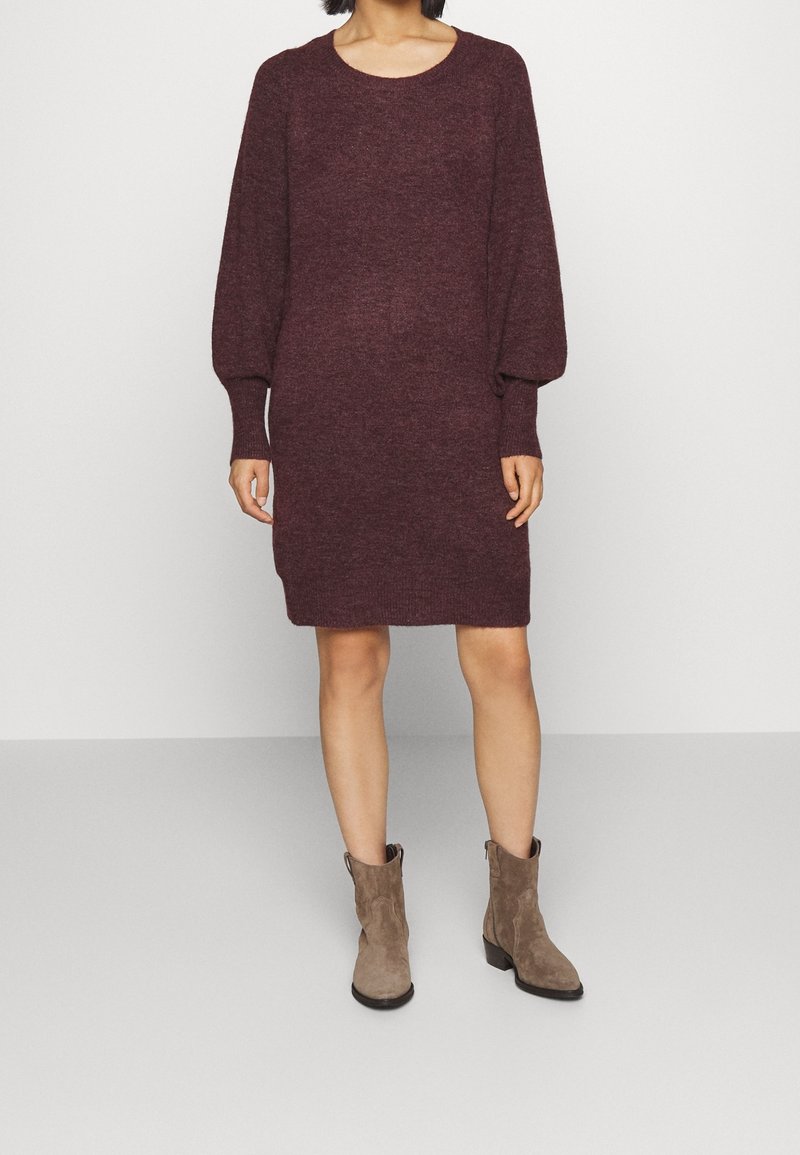 Robe pull en maille bordeaux avec de longues manches bouffantes et un col rond, associée à des bottines en daim marron clair.